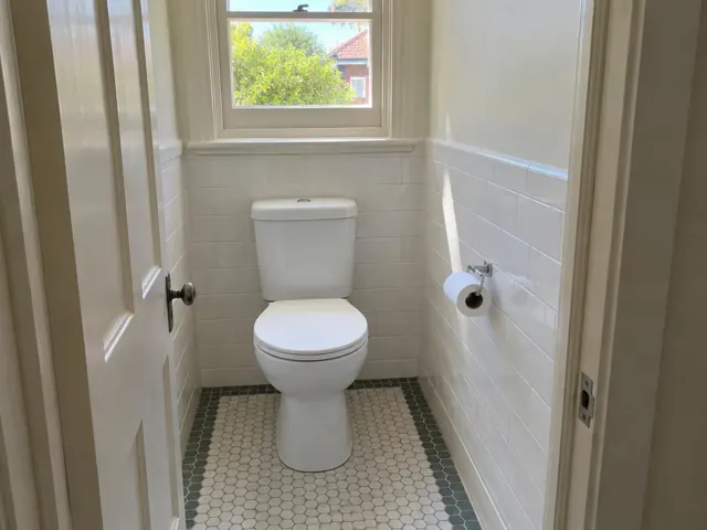 Clean white toilet in a tiled small bathroom with a window and toilet paper holder in Cabarita