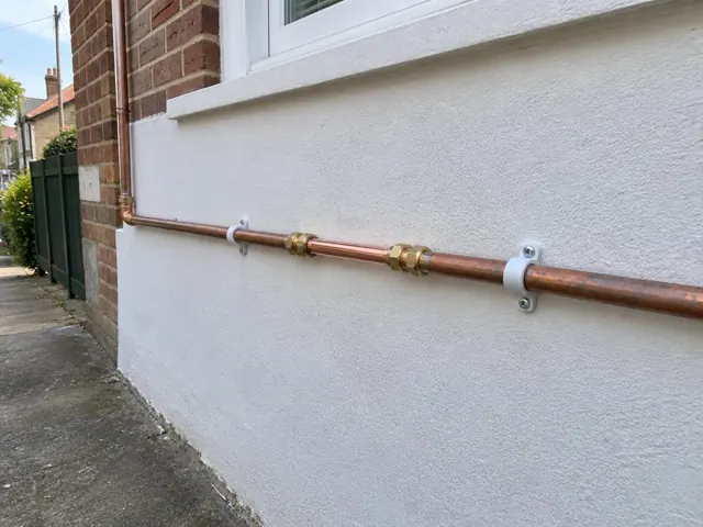 Exposed copper water pipe with repaired coupling on a rendered exterior wall in Drummoyne